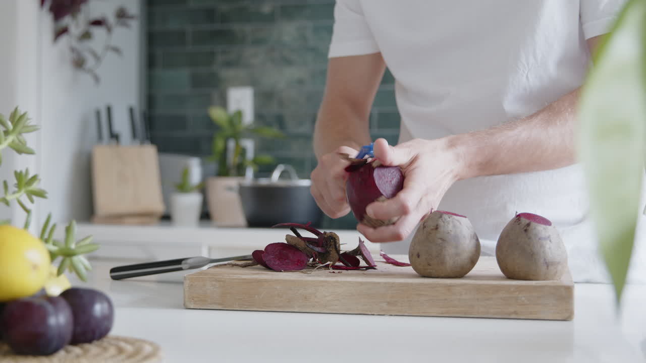 Close-up of a man peeling fresh beetroot with a peeler in a modern kitchen