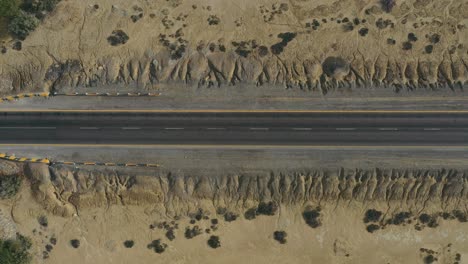 aerial looking down as car passes along empty road through desert landscape in balochistan