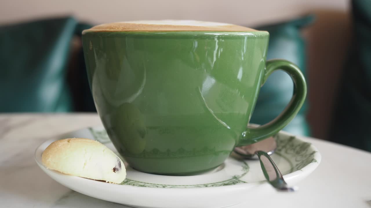 primer plano de una taza de café verde con una galleta en un platillo