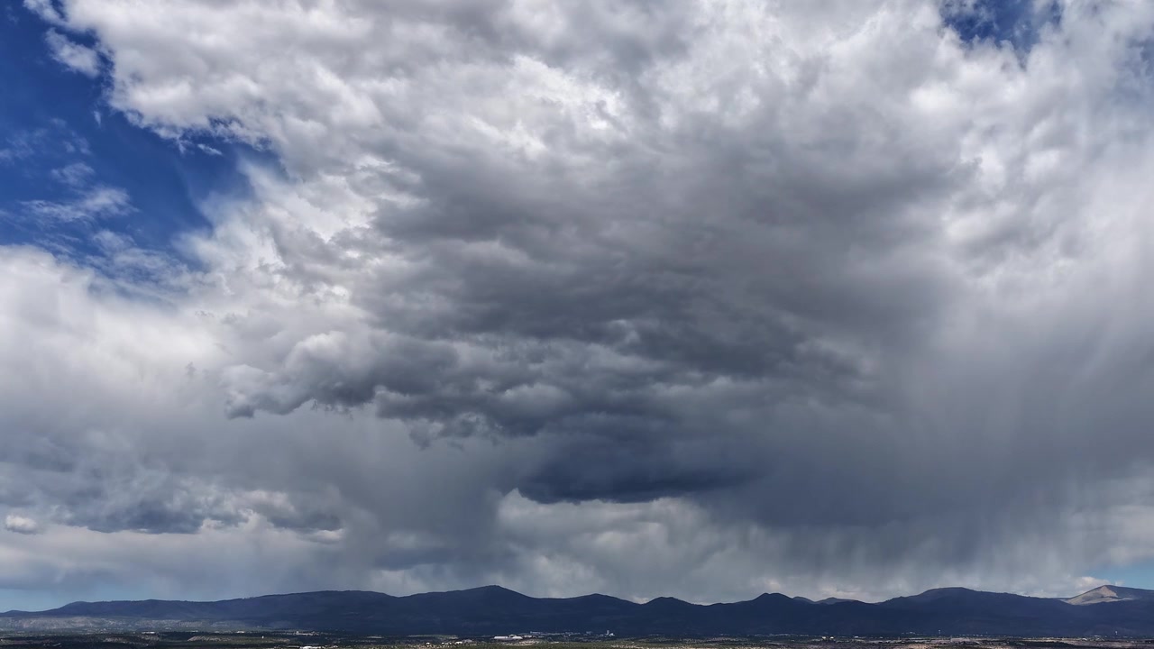 Luftbåren drone-timelapse, der fanger en imponerende monsunstorm. Tunge mørke skyer hvirvler og dannes dynamisk, og udløser kraftige lokale regnbyger over et barskt bjerglandskab