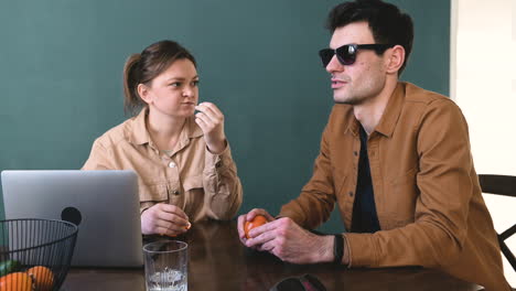 Frau-Und-Blinder-Mann-Mit-Brille-Schälen-Und-Essen-Mandarinen,-Während-Sie-Zu-Hause-Am-Tisch-Sitzen