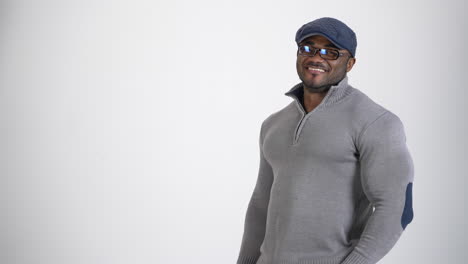 portrait of a handsome african guy. young stylish black man in gray sweater and cap wearing glasses standing in studio and smiling on camera. copy space.