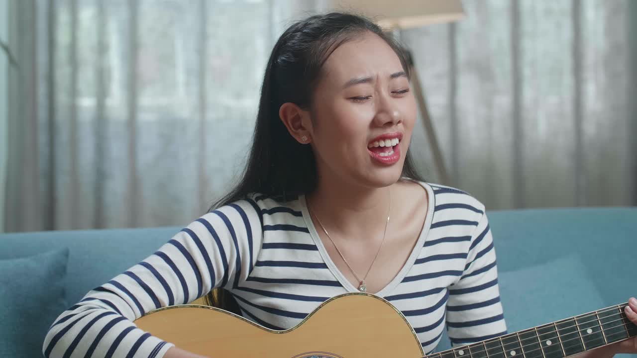 여성이 집에서 노래하고 어쿠스틱 기타를 연주하고 있습니다.