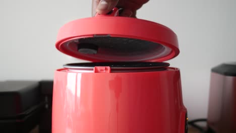 a person opening a pink mini rice cooker lid, followed by a view of the open rice cooker