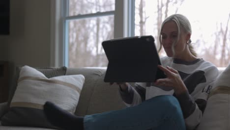 woman-walking-to-the-couch-to-lay-down-and-scroll-through-tablet-while-drinking-coffee-in-a-nice-house