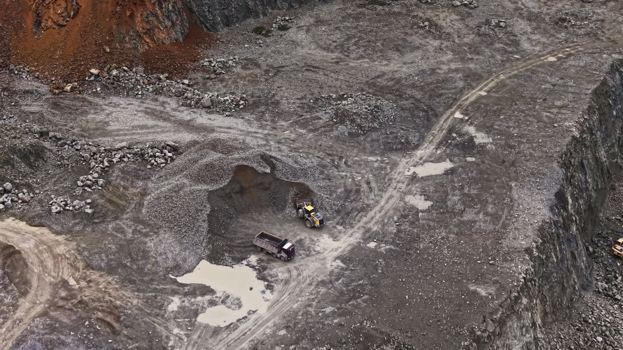 Workers extract granite from a quarry while large machinery operates and processes materials during the day at a mining site