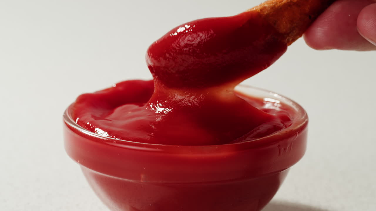 Hand dipping sweet potato fries into ketchup