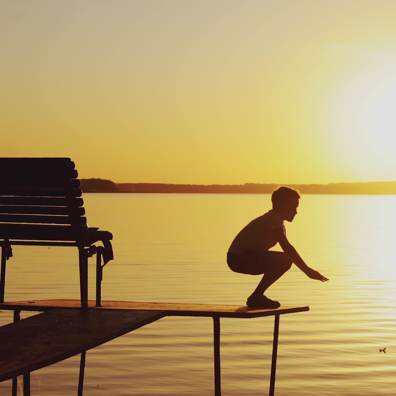 boy are doing physical activities on the bridge near the bench on the background of sunset by the river