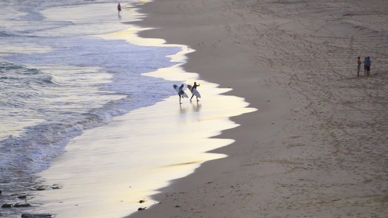 Two surfers exit the water and runoff during sunset at Bar Beach, Newcastle, NSW, Australia