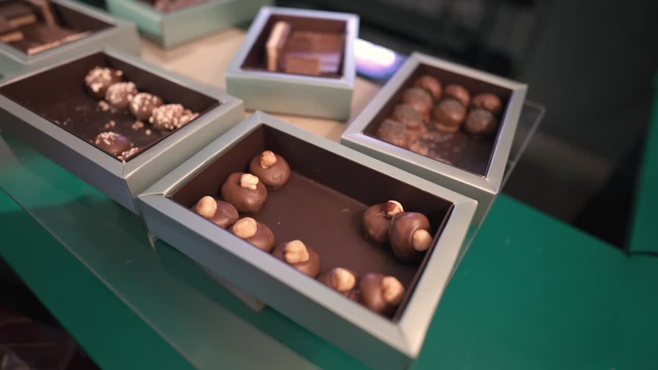 Hand reaches in to arrange round chocolate pieces with whole nuts inside pastel gift boxes, creating an elegant wedding favor display on a glossy surface