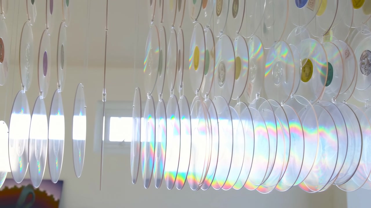 Interior ceiling display of translucent circular discs suspended from thin cords, viewed from slightly low angle with strong backlight, soft reflections, layered pattern, and airy decorative feel