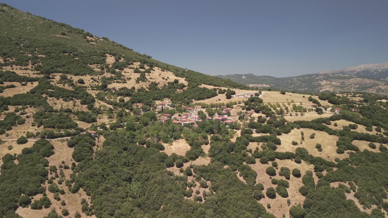 Ripresa in avanti con drone aereo su un tradizionale villaggio greco a Mikros Pontias, circondato da un suggestivo paesaggio montano in una giornata di sole