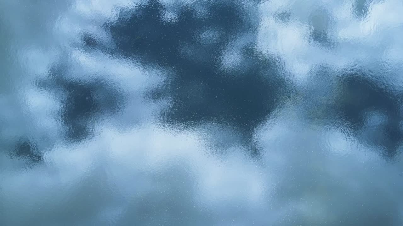 agua ondulada que refleja el sol brillando a través de una formación de nubes distorsionadas contra un cielo azul.