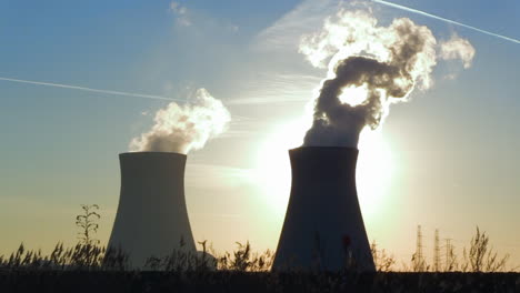 cooling towers with rising vapor, backlit by the setting sun