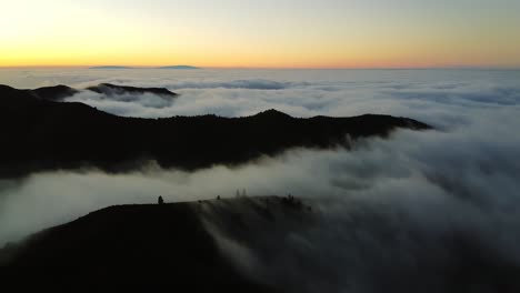 aerial footage over the thick fog or clouds from which only the mountain peaks of the blue sky are visible brightly illuminated