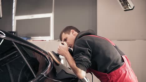 Man-in-red-onezie-polishing-black-car.