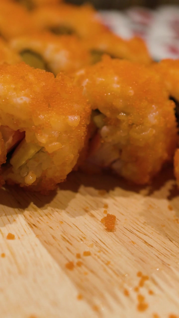 A close-up camera tilt reveals rows of fresh sushi rolls topped with bright orange roe