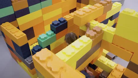 young caucasian white child playing in foam blocks in a padded play area, exploring and stacking large colorful shapes, looking up with happiness, slow motion