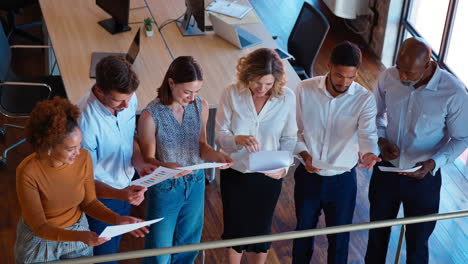 geschäftsfrau leitet ein team-meeting in einem geschäftigen multikulturellen büro und verteilt dokumente