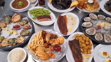 birds eye view of restaurant table full of various seafood dishes from oysters on the half shell to blackened fish to fried shrimp to steamed mussels, over top slider 4k