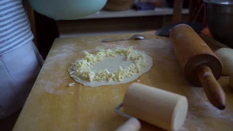 person sprinkling cheese on dough pizza base in home kitchen