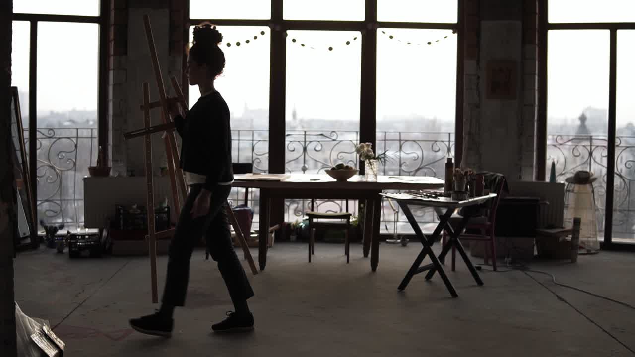 Female slighty unrecognizable figure lifting up the easel and taking it away somewhere in unknown direction.