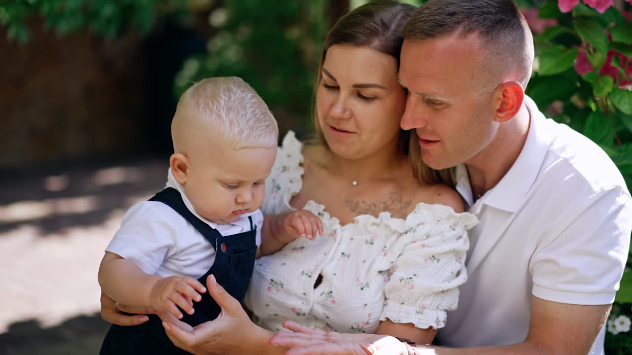 Happy loving parents are outdoors with their child. Daddy shows a plant to his little baby son.