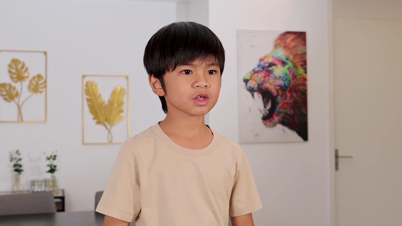 Young boy playfully presses hands together, smiling in bright modern room with colorful wall art