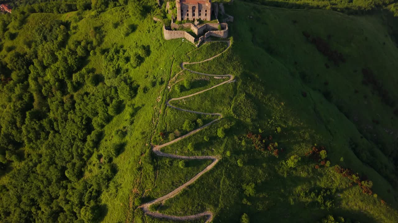 Winding dirt path leading to an ancient fort in Italy, with greenery surrounding it