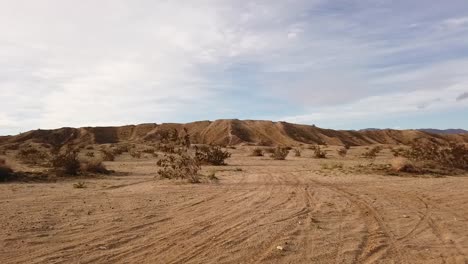 panning view of sandy surface marked with off road vehicle tire tracks and rising hills beyond