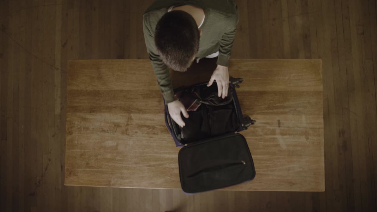 un joven ocupado desempacando y arreglando sus cosas del equipaje después de su viaje - vista superior