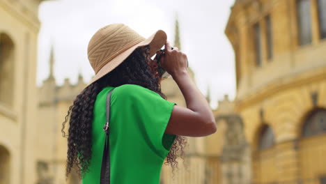 female tourist wearing straw sun hat with camera on vacation in oxford uk exploring city walking taking photos of the sheldonian theatre 2