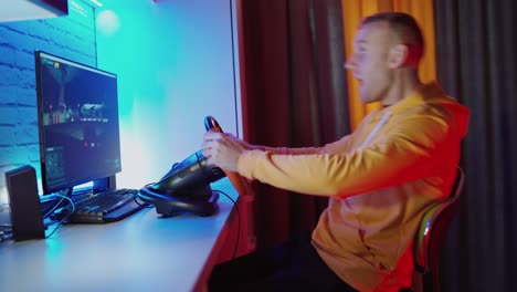 happy man manages steering wheel in front of computer. side view of a young man playing video games at home. modern technology. leisure time concept