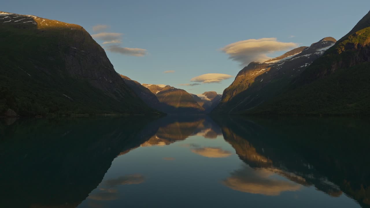 Superbe reflet miroir sur le fjord Lovatnet en Norvège au coucher du soleil, avec des montagnes et des nuages parfaitement reflétés dans une eau calme et limpide.