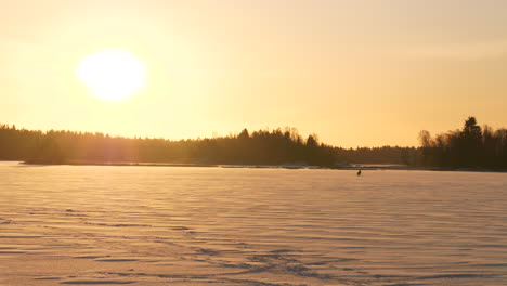 Lonely-man-fishing-on-frozen-lake-in-winter-landscape,-illustrating-the-simple-life-in-Arctic-climate