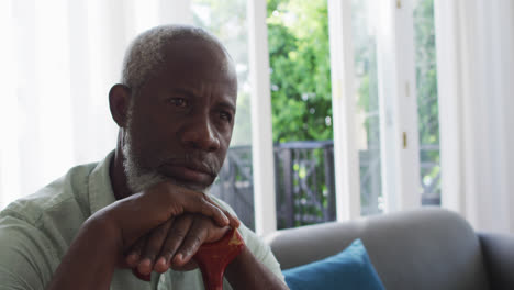 hombre afroamericano sosteniendo un bastón de caminar mientras está sentado en el sofá en casa