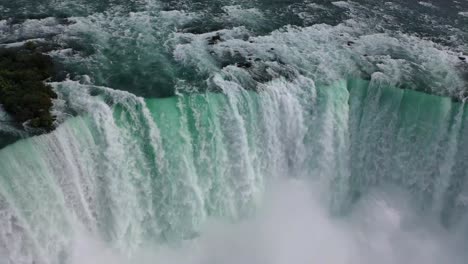 drone captures stunning view of large waterfall plunging into mist-filled gorge in canada, showing turquoise water, strong current, natural beauty, and force of nature from aerial angle.