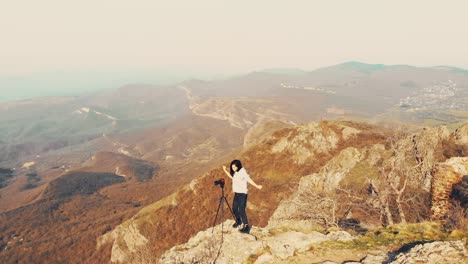 zoom out view attractive caucasian woman photographing in mountains with dslr camera and dancing excited