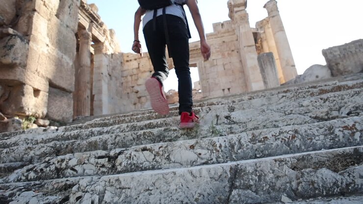 A man in red shoes walks up ancient marble steps