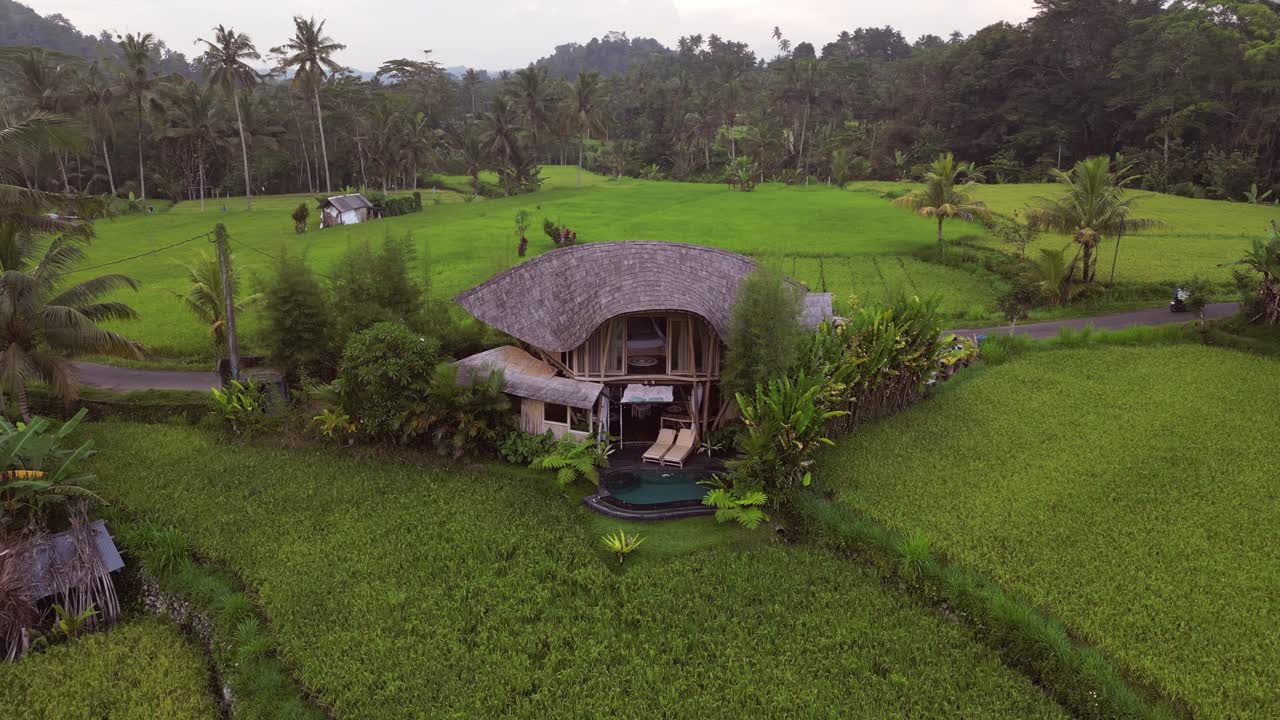 Drone footage of a luxury eco bamboo home with a private pool located in the heart of Ubud, Bali, surrounded by rice terraces, palm trees, and lush tropical plants. A tranquil escape in nature