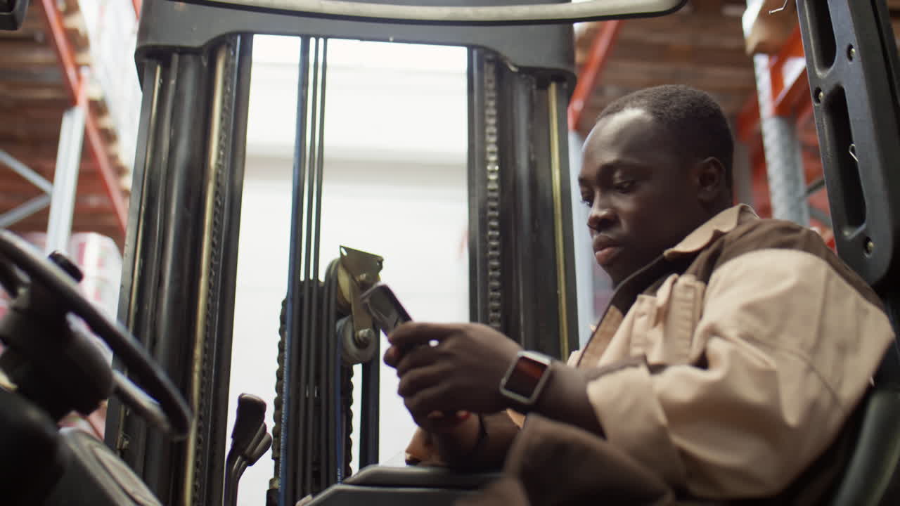 African American man using smartphone in a forklift in a warehouse