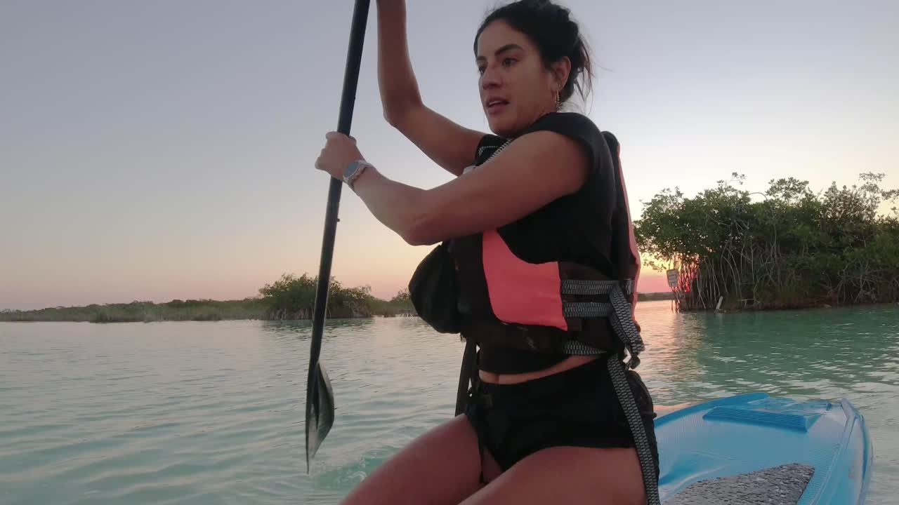 Young woman paddling on a SUP board in Bacalar blue Lagoon Mexico travel destination at sunset, recreational holiday activities