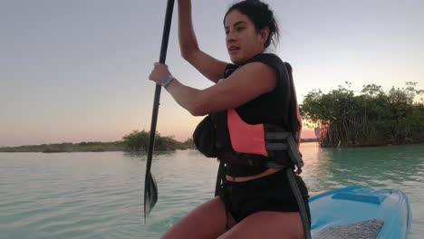 young woman paddling on a sup board in bacalar blue lagoon mexico travel destination at sunset, recreational holiday activities