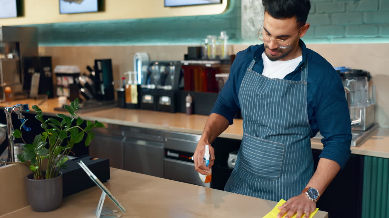 Premium stock video - Waiter man, spray and cleaning table for hygiene