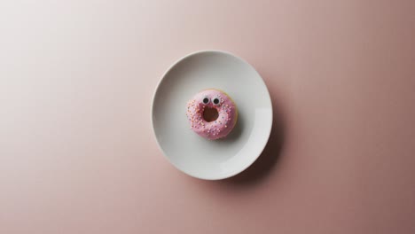 Video-Von-Donut-Mit-Zuckerguss-Auf-Weißem-Teller-Auf-Rosa-Hintergrund