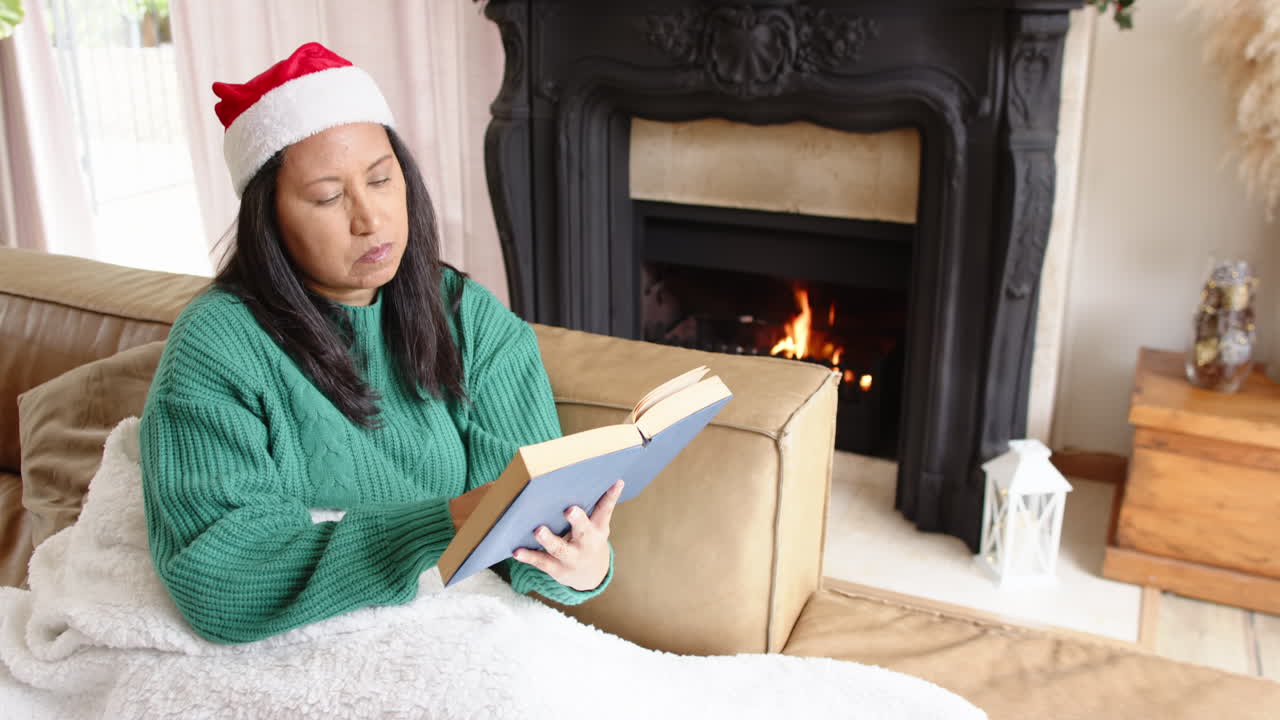 Woman in Santa hat reading book by cozy fireplace during Christmas