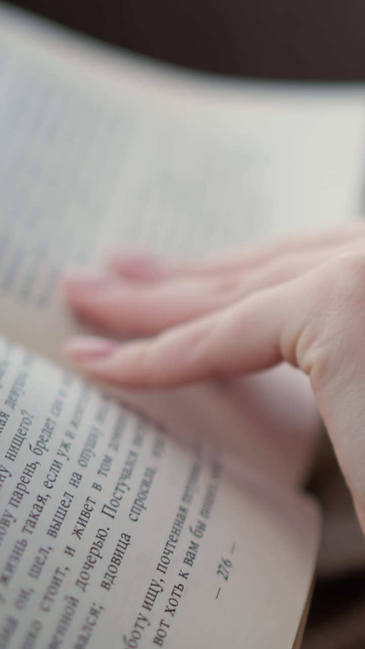 은 옷을 입은 여성이 책의 다음 페이지를 돌리는 클로즈업, 편안하고 편안한 분위기는 그녀의 뜨개질 옷의 부드러운 질감에 초점을 맞추며 조용한 독서를 강조합니다.