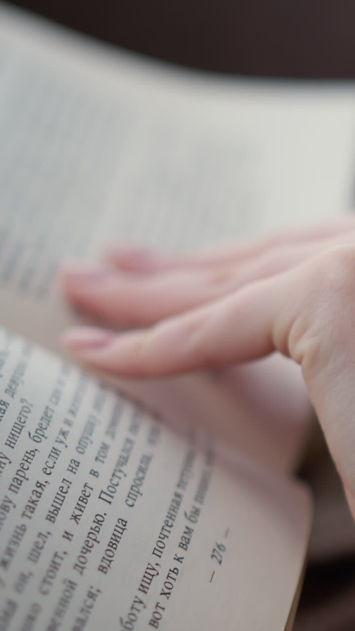 Close-up of lady in woven clothing turning to the next page of a book, the cozy and relaxed atmosphere emphasizes quiet reading with a focus on the soft texture of her knitted garment