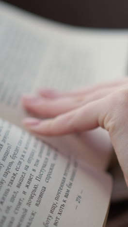primer plano de una mujer con ropa tejida abriendo la siguiente página de un libro, el ambiente acogedor y relajado hace hincapié en la lectura tranquila con un enfoque en la textura suave de su prenda de punto