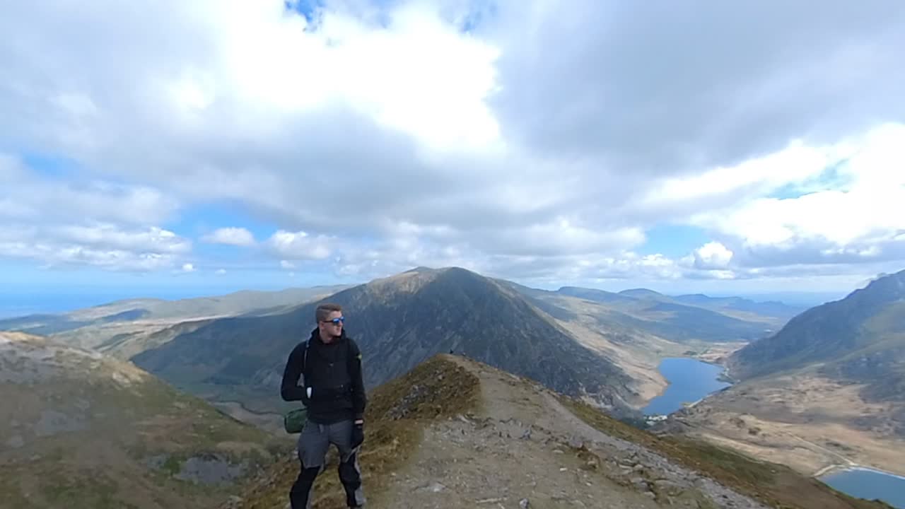 Man stands confidently on narrow Y Garn summit ridge with wide views of mountains, lakes, and sky in Snowdonia national park showing adventure, nature, and peaceful highland atmosphere